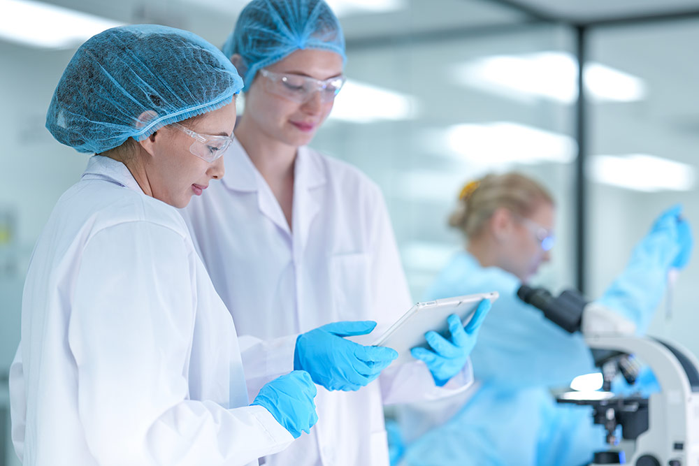 Two people in lab coats looking at a tablet
